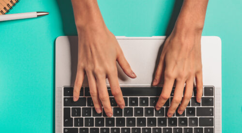 Overhead view of the working woman hands typing on keyboard notebook laptop computer at office desk
