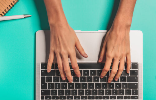 Overhead view of the working woman hands typing on keyboard notebook laptop computer at office desk