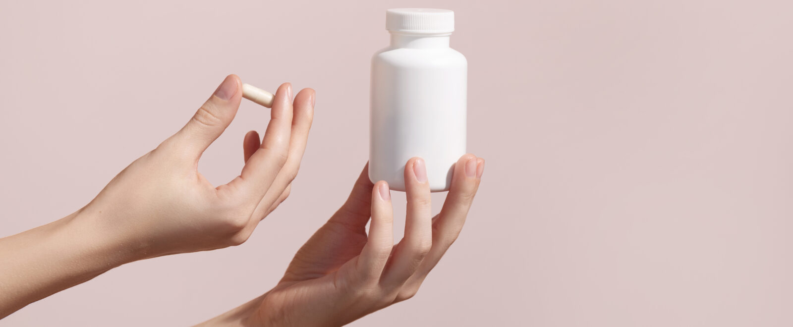 Woman holding pill and blank white plastic tube on pink background