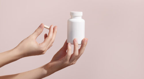 Woman holding pill and blank white plastic tube on pink background