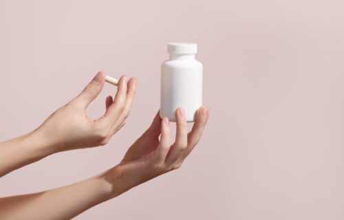 Woman holding pill and blank white plastic tube on pink background