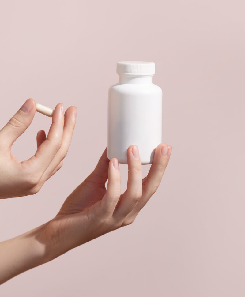 Woman holding pill and blank white plastic tube on pink background