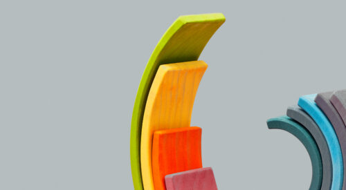 Balanced constructor from colorful curved wooden planks in the form of spiral figure on a light pink background with soft shadows